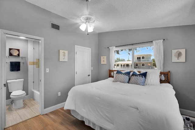 bedroom featuring visible vents, baseboards, vaulted ceiling, wood finished floors, and a textured ceiling