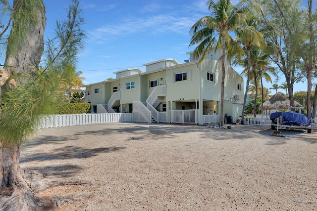 rear view of property featuring stucco siding, stairs, and fence