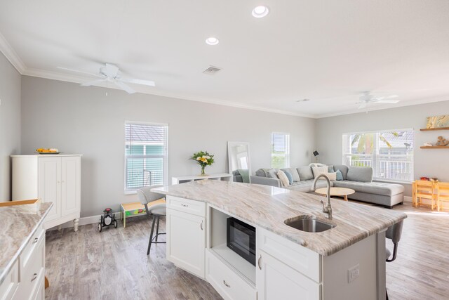 kitchen featuring a breakfast bar, sink, white cabinets, light stone countertops, and a center island with sink