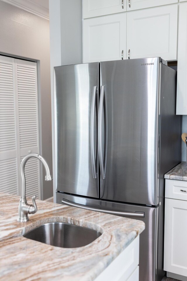 kitchen with sink, stainless steel fridge, white cabinetry, light stone counters, and ornamental molding