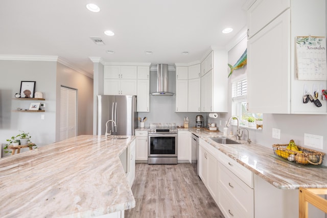 kitchen with sink, appliances with stainless steel finishes, light stone counters, white cabinets, and wall chimney exhaust hood