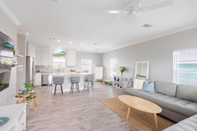 living room featuring crown molding, a wealth of natural light, ceiling fan, and light hardwood / wood-style flooring