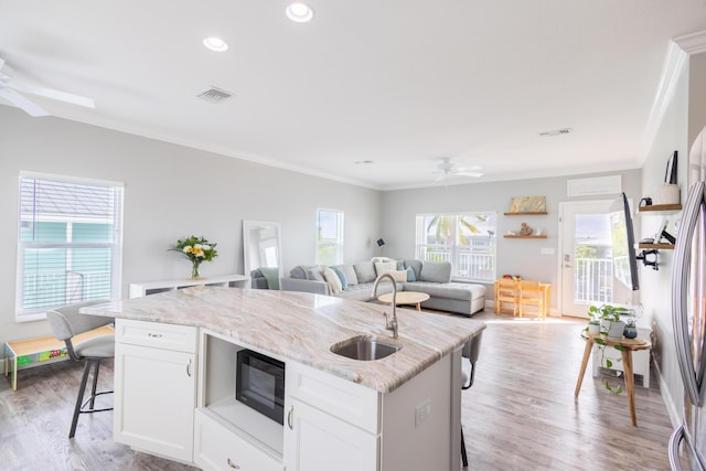 kitchen with sink, a breakfast bar, ceiling fan, white cabinetry, and an island with sink