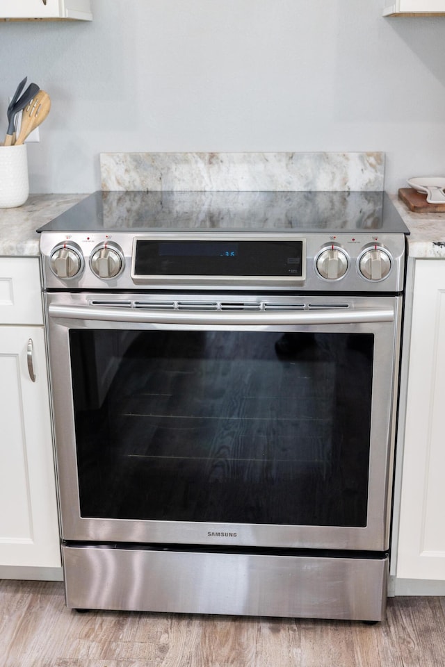 room details featuring light wood-type flooring, white cabinets, and electric range