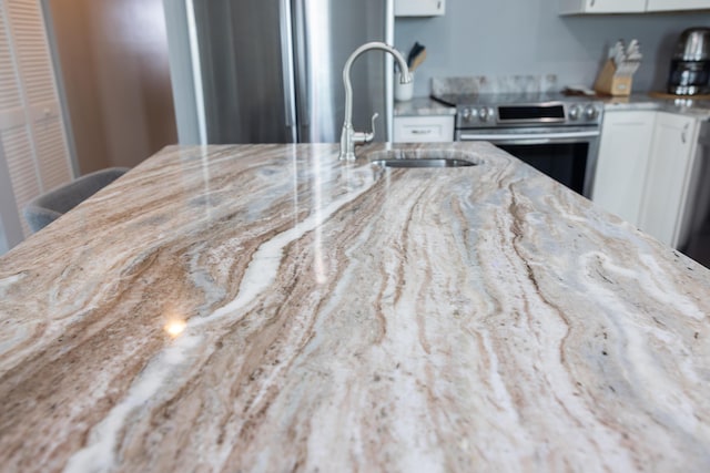 kitchen featuring white cabinetry, sink, stainless steel electric range, and light stone countertops