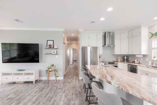 kitchen with appliances with stainless steel finishes, a breakfast bar, white cabinets, light stone counters, and wall chimney exhaust hood