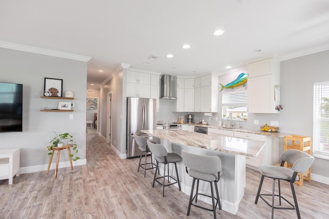 kitchen featuring a breakfast bar, white cabinetry, stainless steel fridge, a center island, and wall chimney range hood