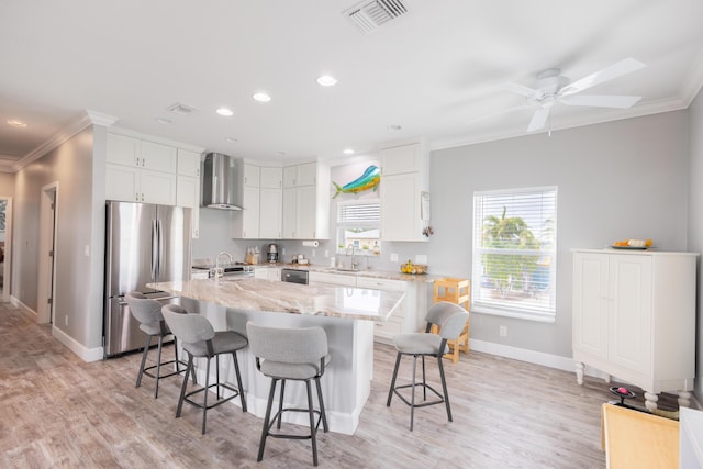 kitchen featuring a breakfast bar area, white cabinetry, stainless steel appliances, a center island, and wall chimney exhaust hood