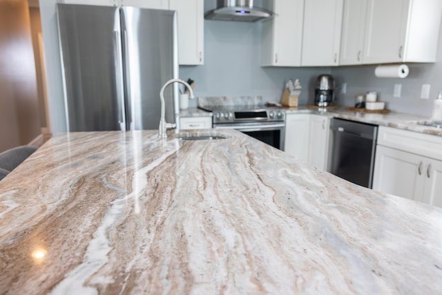 kitchen featuring wall chimney exhaust hood, sink, white cabinetry, stainless steel appliances, and light stone countertops