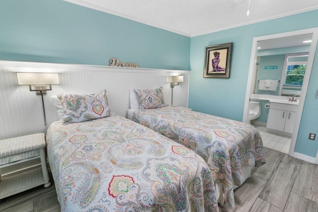 bedroom featuring sink, ornamental molding, light hardwood / wood-style floors, and ensuite bathroom