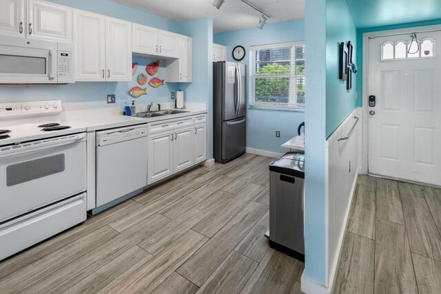 kitchen featuring white cabinetry, rail lighting, sink, and white appliances