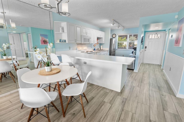 kitchen featuring white cabinets, hanging light fixtures, white appliances, kitchen peninsula, and a textured ceiling