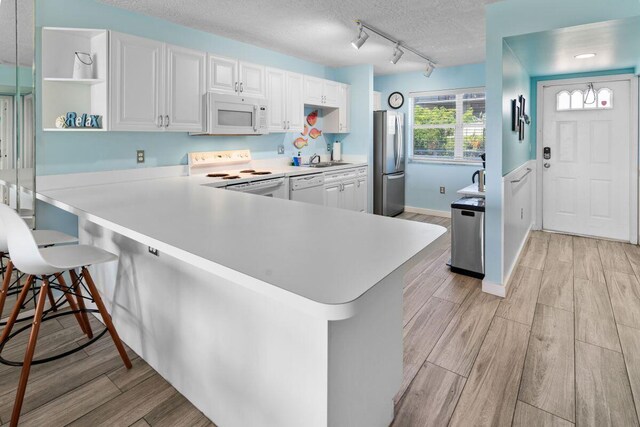 kitchen with white appliances, kitchen peninsula, a breakfast bar area, and white cabinets