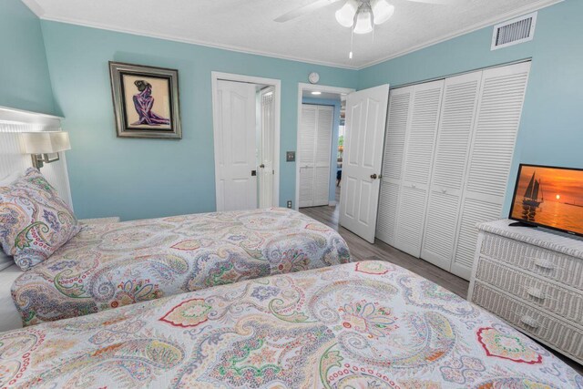 bedroom with hardwood / wood-style flooring, ornamental molding, multiple closets, and ceiling fan