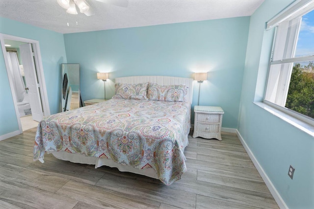 bedroom featuring ceiling fan, ensuite bath, a textured ceiling, and light wood-type flooring