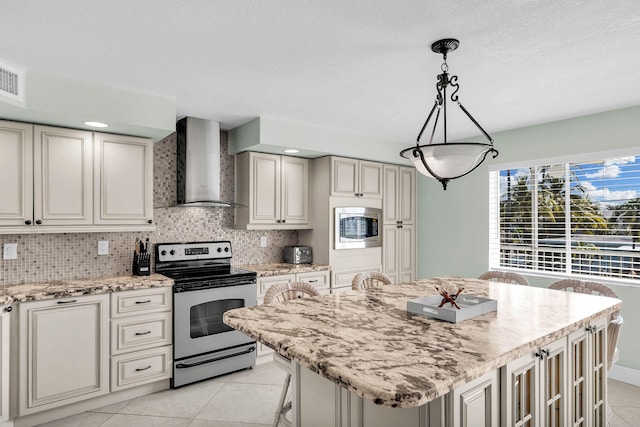 kitchen with light stone counters, a center island, appliances with stainless steel finishes, pendant lighting, and wall chimney range hood