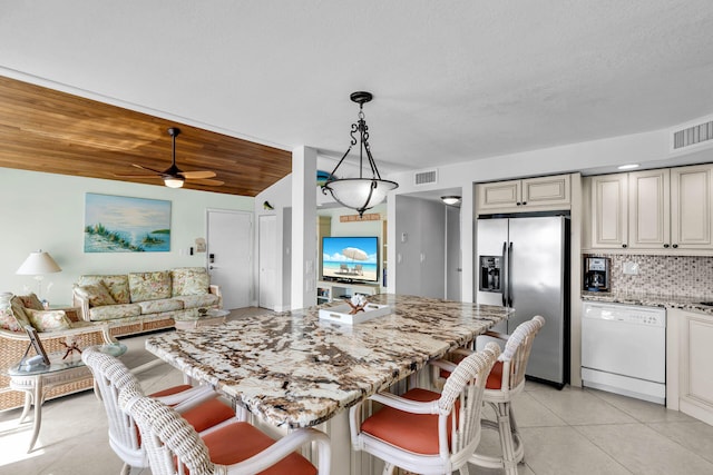 kitchen featuring a kitchen bar, hanging light fixtures, stainless steel fridge, dishwasher, and backsplash