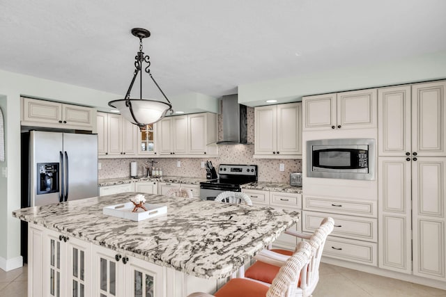 kitchen with appliances with stainless steel finishes, a kitchen island, light stone countertops, a kitchen bar, and wall chimney exhaust hood