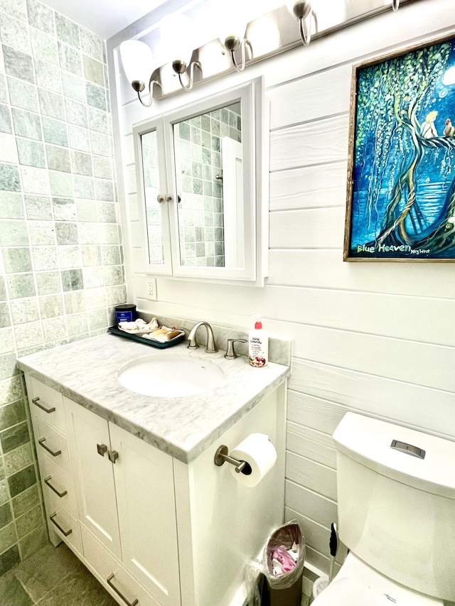 bathroom with vanity, toilet, and tile walls