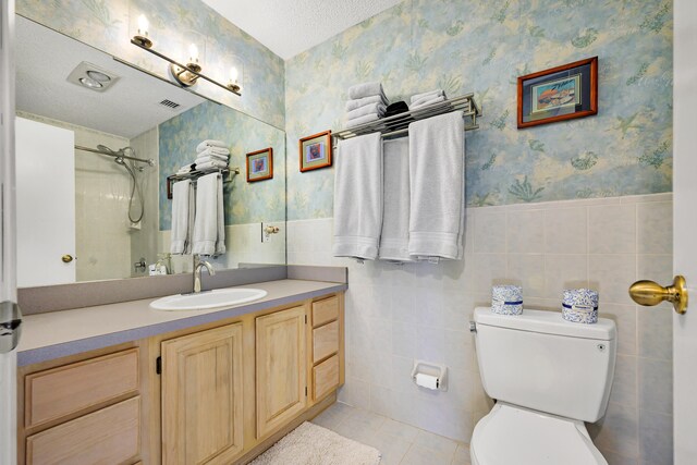 bathroom with vanity, tile walls, toilet, and tiled shower