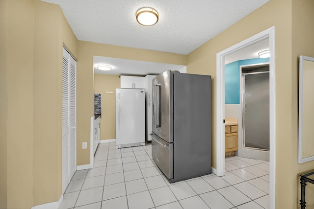 kitchen with white cabinetry, a textured ceiling, light tile patterned floors, white refrigerator, and stainless steel fridge