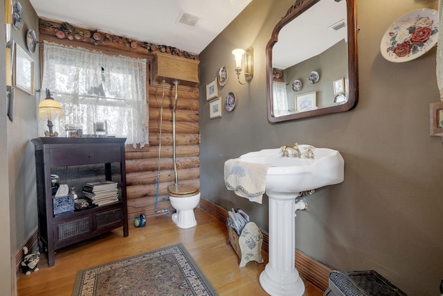 bathroom featuring log walls, toilet, and hardwood / wood-style flooring