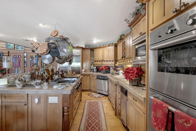 kitchen featuring light brown cabinets, vaulted ceiling, light hardwood / wood-style floors, and appliances with stainless steel finishes