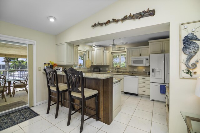 kitchen featuring lofted ceiling, light tile patterned floors, white appliances, cream cabinets, and a kitchen bar