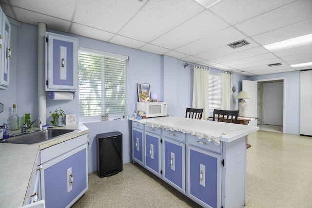 kitchen with blue cabinetry, a paneled ceiling, a breakfast bar, and sink