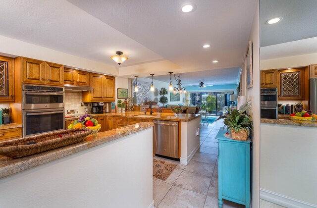 kitchen with light tile patterned floors, appliances with stainless steel finishes, kitchen peninsula, pendant lighting, and backsplash