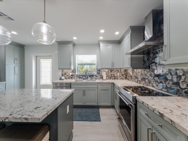 kitchen with pendant lighting, sink, gray cabinets, stainless steel appliances, and wall chimney exhaust hood