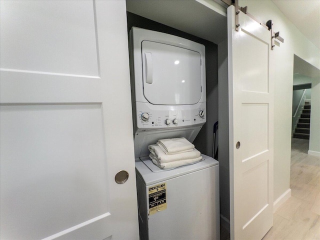 laundry room with light hardwood / wood-style flooring, a barn door, and stacked washer / dryer