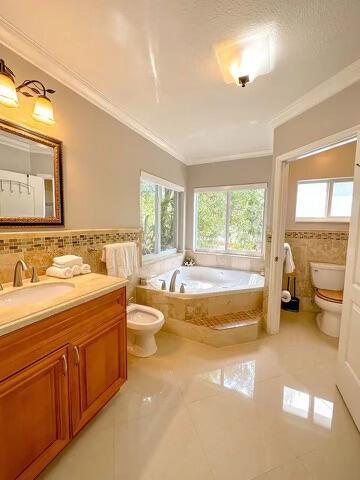 bathroom with tile walls, tiled bath, toilet, crown molding, and tile patterned floors