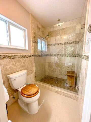 bathroom featuring tile walls, tile patterned flooring, a shower with shower door, and toilet