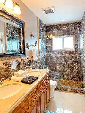 bathroom with a tile shower, tile walls, vanity, and toilet