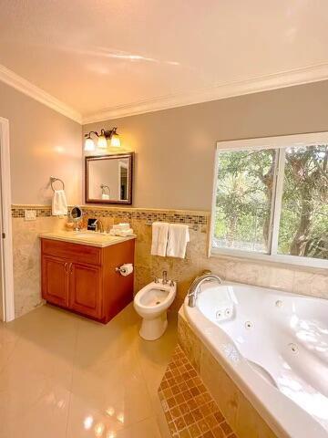 bathroom with a bidet, tiled tub, tile walls, vanity, and ornamental molding