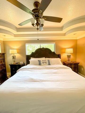 bedroom with crown molding, a tray ceiling, and ceiling fan