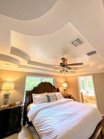 bedroom with a raised ceiling, ceiling fan, ensuite bathroom, and a textured ceiling