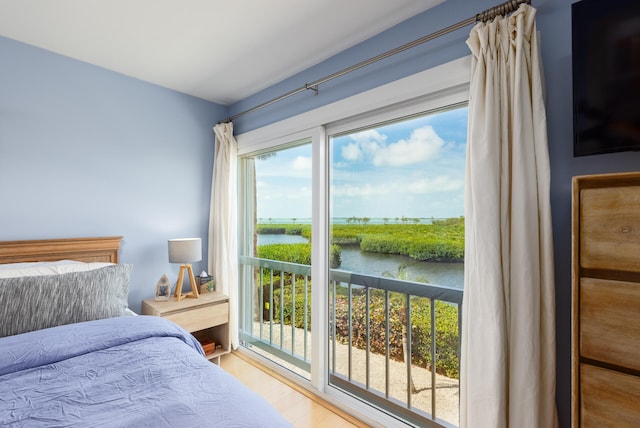 bedroom featuring access to exterior, hardwood / wood-style floors, and a water view