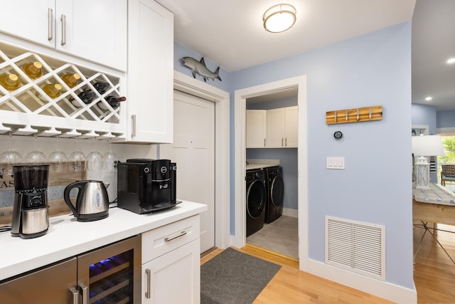 kitchen featuring light hardwood / wood-style flooring, washer and clothes dryer, wine cooler, bar, and white cabinets