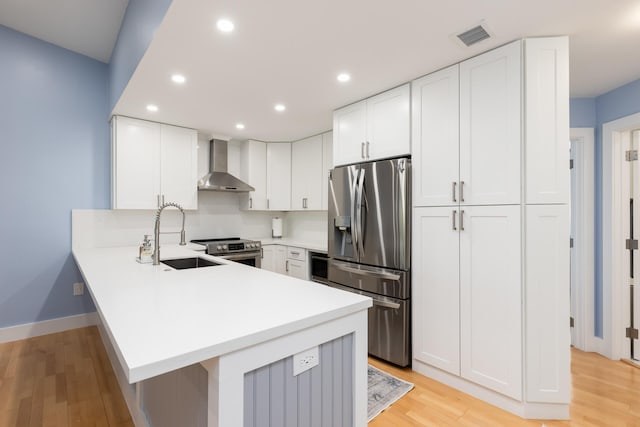 kitchen with sink, stainless steel appliances, white cabinetry, and wall chimney range hood