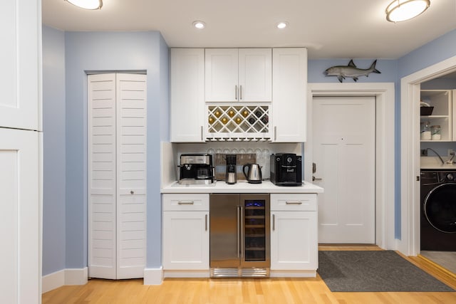 kitchen with white cabinetry, light hardwood / wood-style flooring, indoor bar, washer / clothes dryer, and beverage cooler