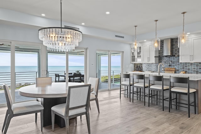 dining room featuring a water view, sink, an inviting chandelier, and light wood-type flooring