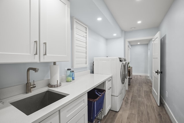 washroom with cabinets, sink, washing machine and dryer, and light hardwood / wood-style flooring