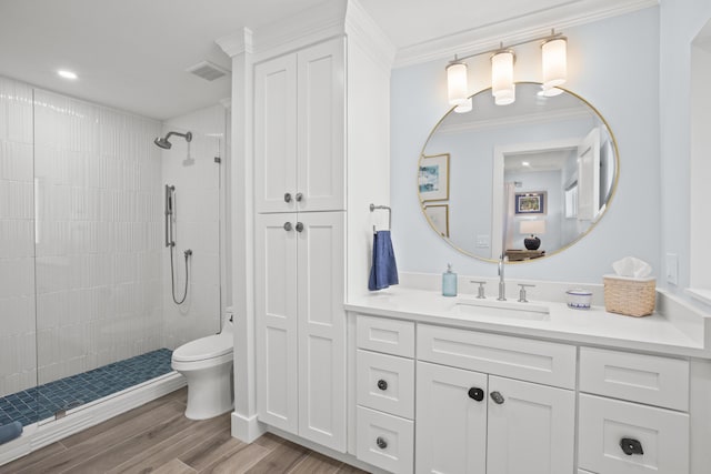 bathroom featuring toilet, a tile shower, ornamental molding, vanity, and hardwood / wood-style floors