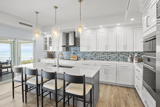 kitchen featuring sink, a breakfast bar, white cabinets, a center island with sink, and wall chimney exhaust hood