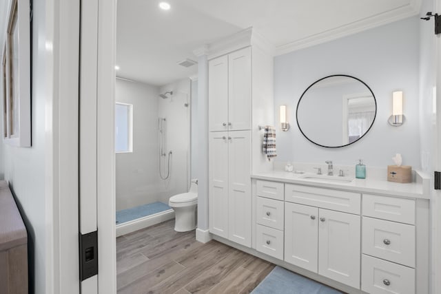 bathroom featuring a tile shower, wood-type flooring, vanity, toilet, and crown molding