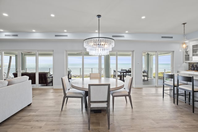 dining space featuring a water view, an inviting chandelier, and light hardwood / wood-style floors