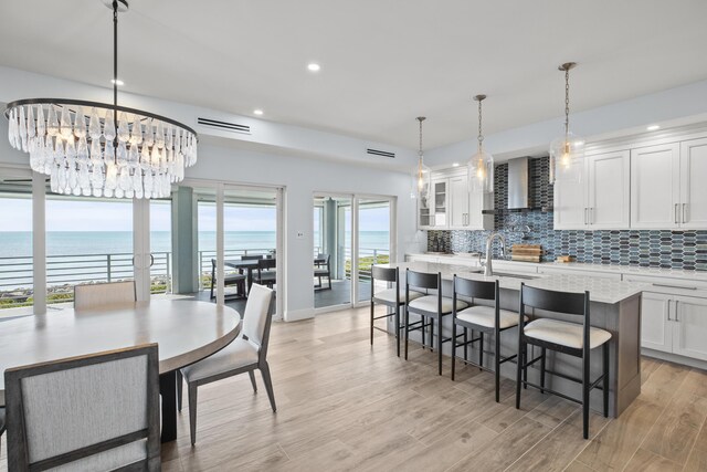 dining area with a water view, light hardwood / wood-style floors, sink, and a notable chandelier