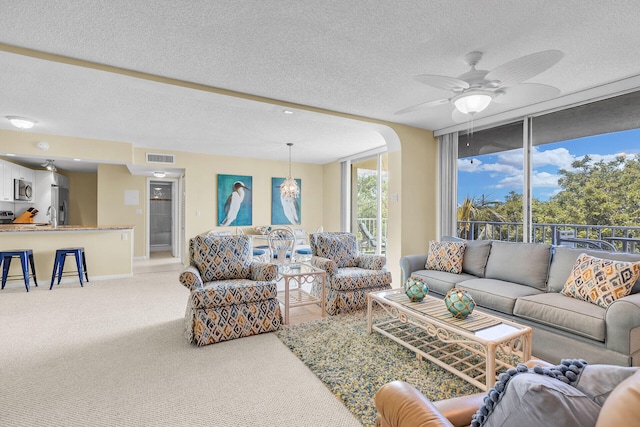 carpeted living room featuring a ceiling fan, arched walkways, visible vents, and a textured ceiling